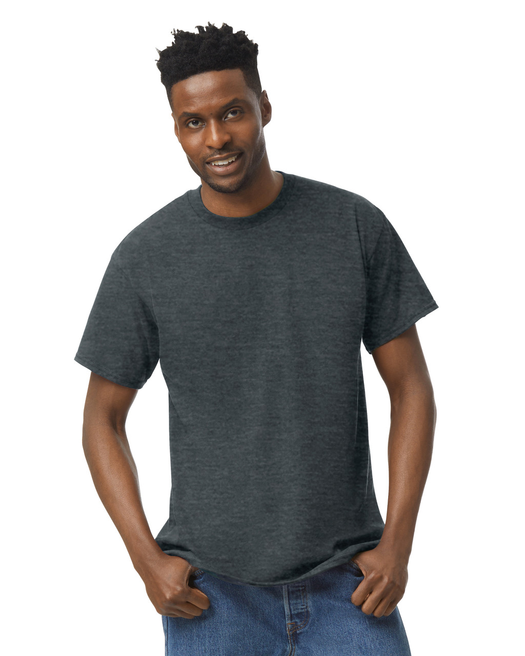 Smiling man with short curly hair, three-quarter pose with thumbs hooked in jeans pockets, wearing a plain dark heather grey crew-neck t-shirt, on a plain white studio background.